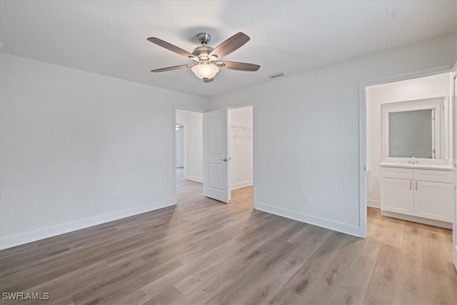 unfurnished bedroom with sink, light hardwood / wood-style flooring, ceiling fan, a walk in closet, and a closet