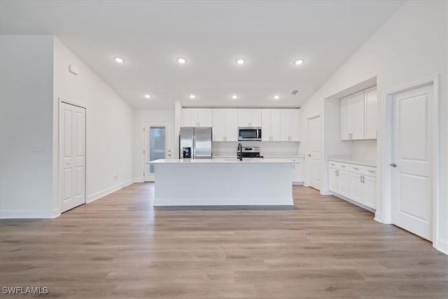 kitchen featuring lofted ceiling, white cabinetry, a center island with sink, stainless steel appliances, and light hardwood / wood-style floors