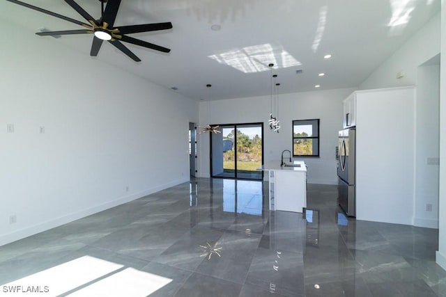 interior space featuring pendant lighting, sink, stainless steel fridge, white cabinets, and a center island with sink