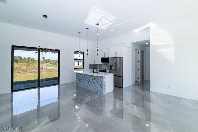 kitchen featuring white cabinetry, a center island with sink, appliances with stainless steel finishes, pendant lighting, and decorative backsplash