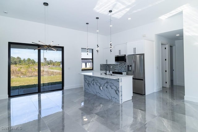 kitchen with appliances with stainless steel finishes, pendant lighting, white cabinetry, light stone counters, and a center island with sink