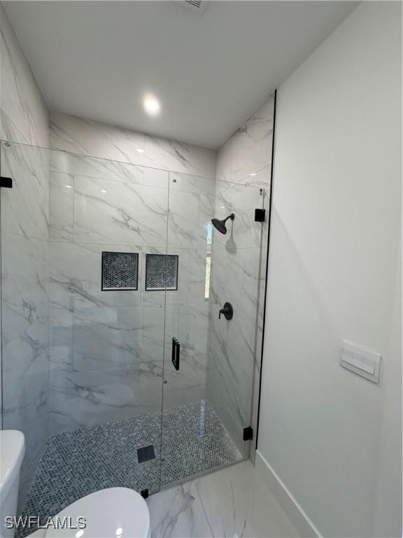 bathroom featuring a marble finish shower, marble finish floor, toilet, and baseboards