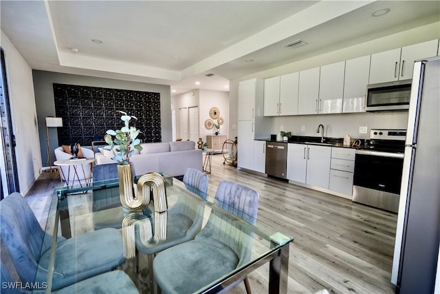 dining room with sink, light hardwood / wood-style flooring, and a raised ceiling