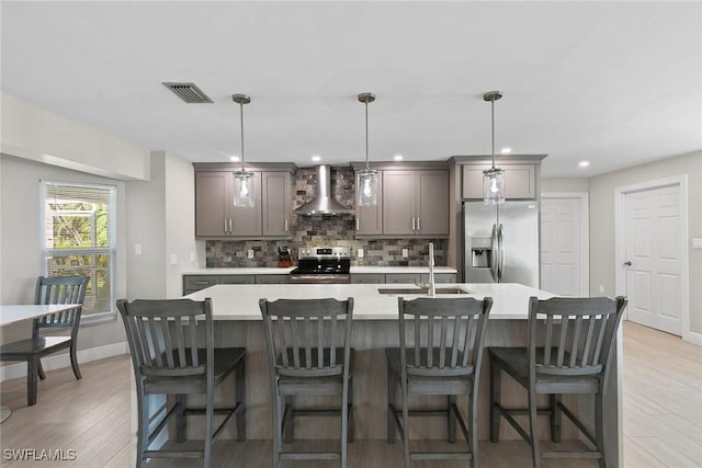 kitchen with a center island with sink, appliances with stainless steel finishes, sink, and wall chimney range hood