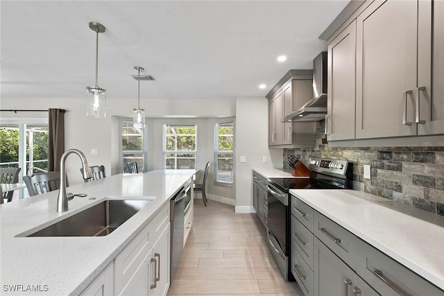 kitchen featuring appliances with stainless steel finishes, decorative light fixtures, sink, light stone counters, and wall chimney range hood