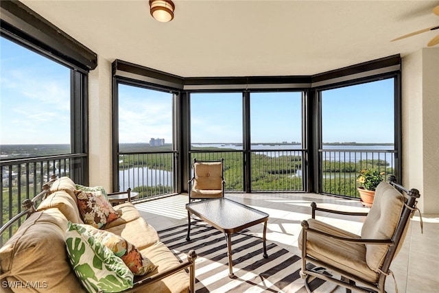 sunroom with a healthy amount of sunlight, ceiling fan, and a water view