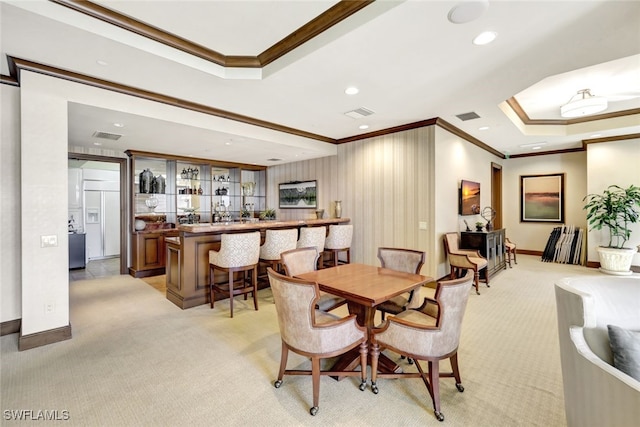 carpeted dining space with a raised ceiling, crown molding, and bar