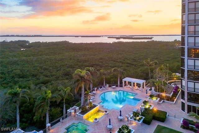 pool at dusk featuring a patio area, a community pool, a water view, and a pergola