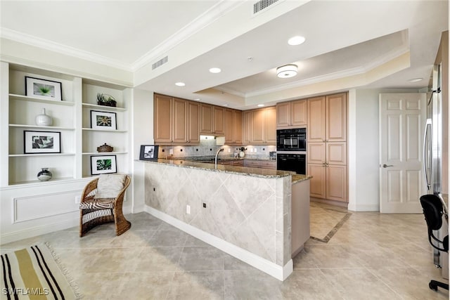 kitchen with a tray ceiling, a peninsula, visible vents, and ornamental molding