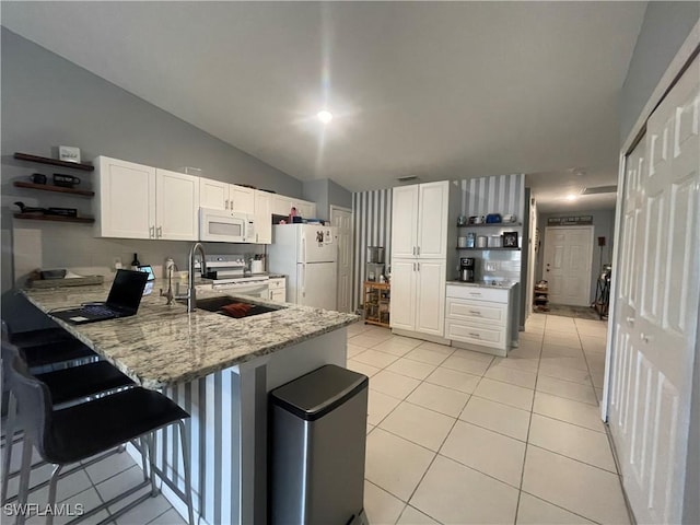 kitchen with a breakfast bar, white cabinetry, light tile patterned floors, light stone counters, and white appliances