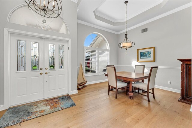 entryway featuring an inviting chandelier, ornamental molding, a tray ceiling, and light hardwood / wood-style flooring