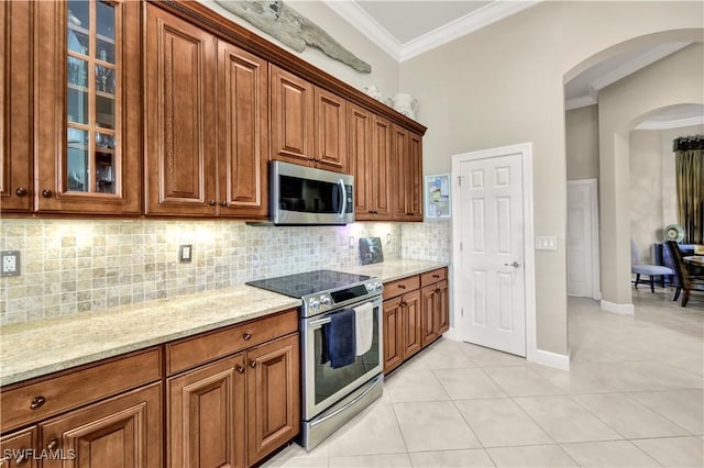 kitchen featuring light tile patterned flooring, ornamental molding, light stone countertops, and appliances with stainless steel finishes