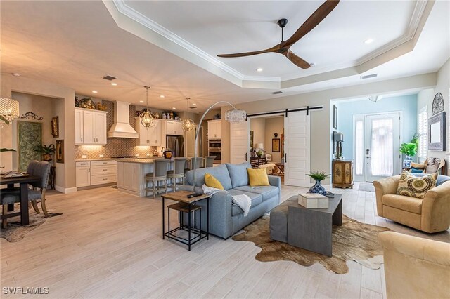 living room with crown molding, a tray ceiling, a barn door, and light hardwood / wood-style flooring