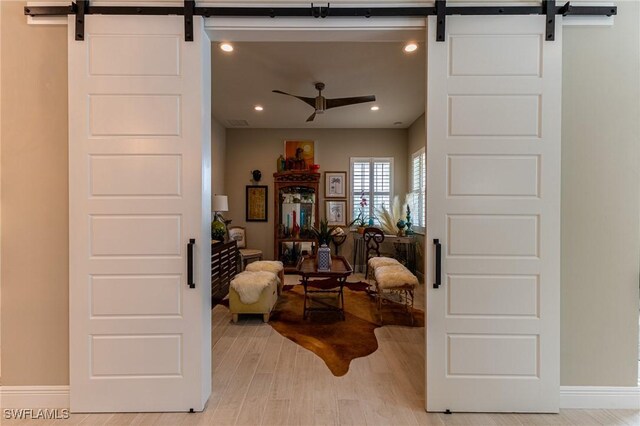 sitting room featuring ceiling fan, a barn door, and light wood-type flooring