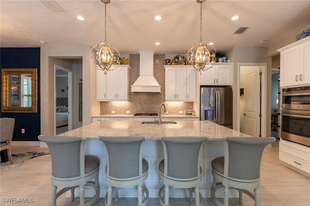 kitchen with pendant lighting, sink, custom exhaust hood, a kitchen island with sink, and stainless steel appliances