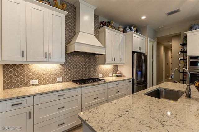 kitchen with sink, custom range hood, white cabinets, and appliances with stainless steel finishes