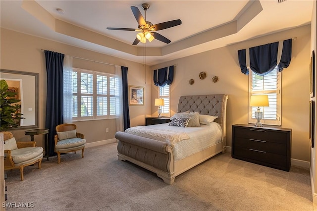 bedroom with light carpet, baseboards, a tray ceiling, and a ceiling fan