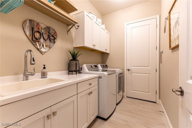 clothes washing area with cabinet space, baseboards, light wood-style flooring, independent washer and dryer, and a sink