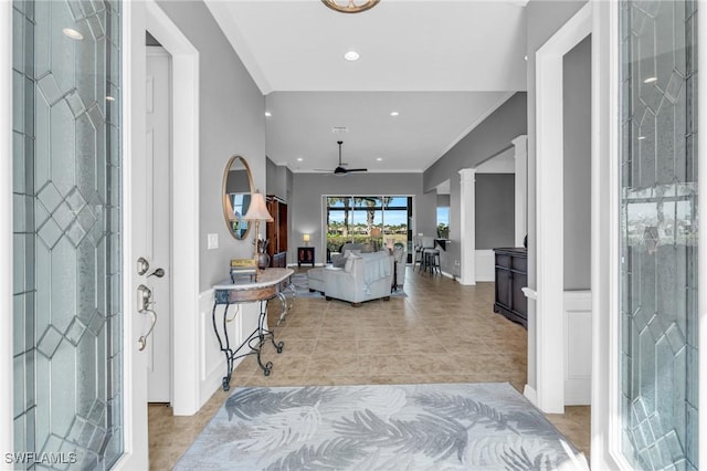 foyer entrance featuring crown molding, ceiling fan, light tile patterned flooring, and ornate columns