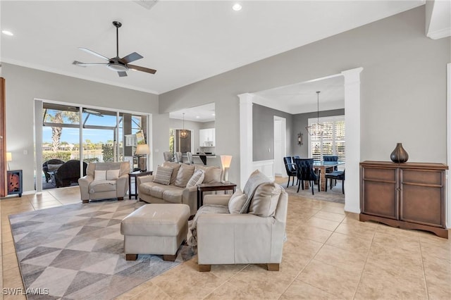 living room featuring light tile patterned flooring, crown molding, ceiling fan with notable chandelier, and ornate columns