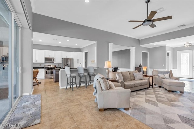 tiled living room featuring crown molding, ceiling fan, and ornate columns