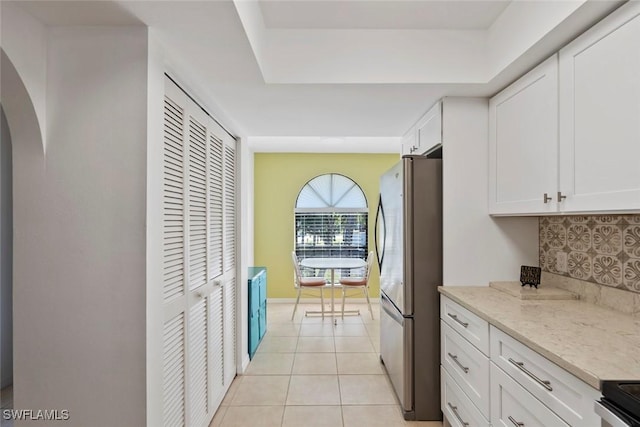 kitchen featuring light tile patterned floors, electric range oven, decorative backsplash, freestanding refrigerator, and white cabinetry