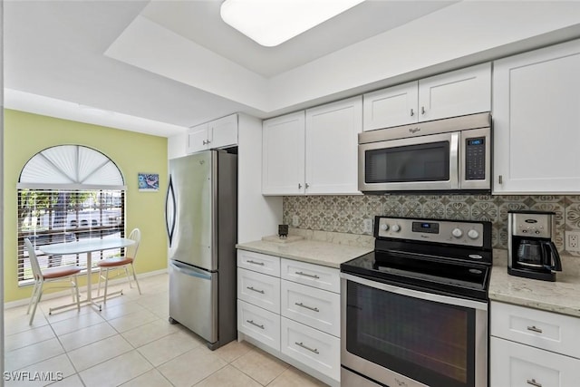 kitchen with tasteful backsplash, white cabinets, appliances with stainless steel finishes, light stone countertops, and light tile patterned flooring