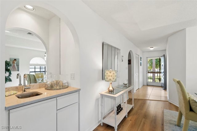 hallway with arched walkways, light wood-style floors, plenty of natural light, and a sink