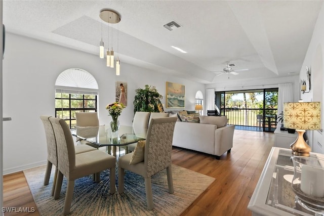 dining room with dark wood-type flooring, ceiling fan, a tray ceiling, and a textured ceiling