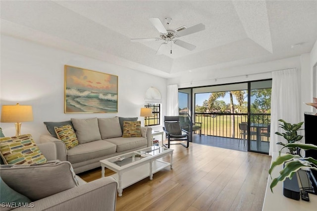 living room featuring ceiling fan, a textured ceiling, light wood-style floors, and a raised ceiling
