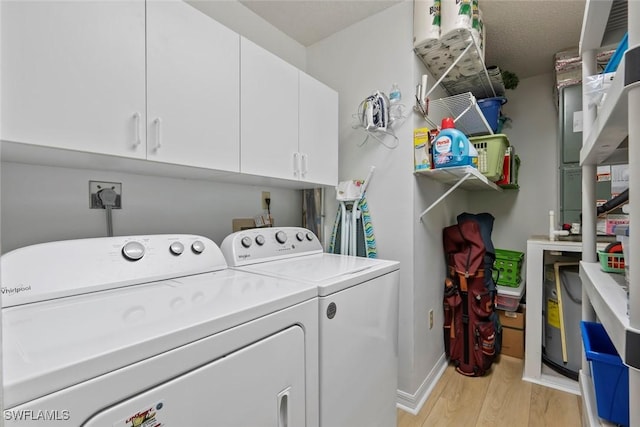 clothes washing area with cabinet space, light wood-style floors, washing machine and clothes dryer, and baseboards