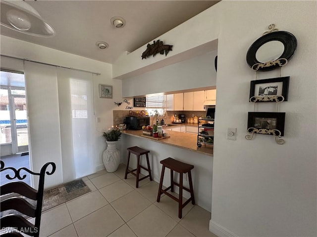 kitchen featuring white cabinetry, backsplash, a kitchen breakfast bar, light tile patterned floors, and kitchen peninsula