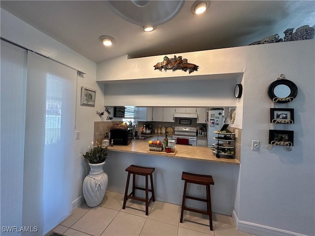 kitchen with a breakfast bar, refrigerator, stainless steel range with electric stovetop, tasteful backsplash, and kitchen peninsula