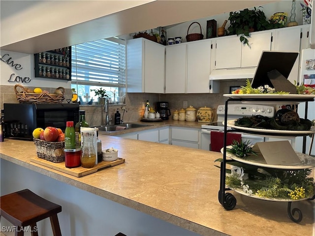 kitchen featuring white electric stove, tasteful backsplash, sink, and white cabinets