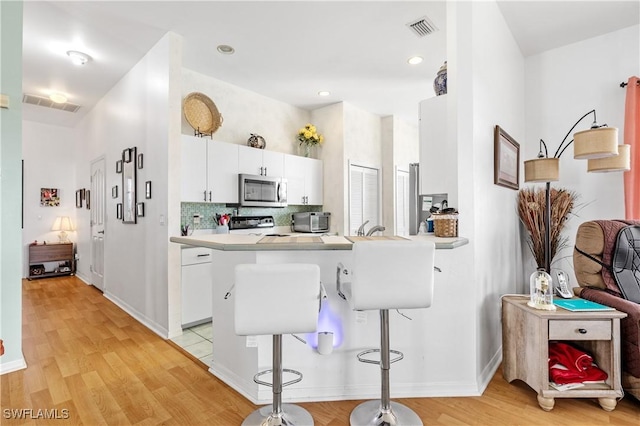 kitchen featuring stove, kitchen peninsula, a breakfast bar, and white cabinets