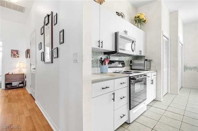 kitchen with electric stove, light tile patterned floors, tasteful backsplash, and white cabinets