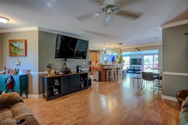 living room with ornamental molding, ceiling fan, a textured ceiling, and light hardwood / wood-style flooring