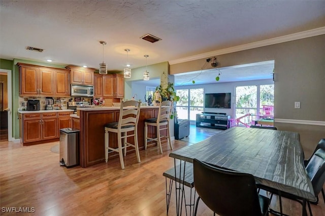 kitchen featuring appliances with stainless steel finishes, a kitchen bar, hanging light fixtures, ornamental molding, and light wood-type flooring