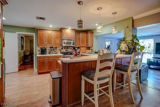 kitchen featuring stainless steel appliances, pendant lighting, a kitchen bar, and light hardwood / wood-style flooring