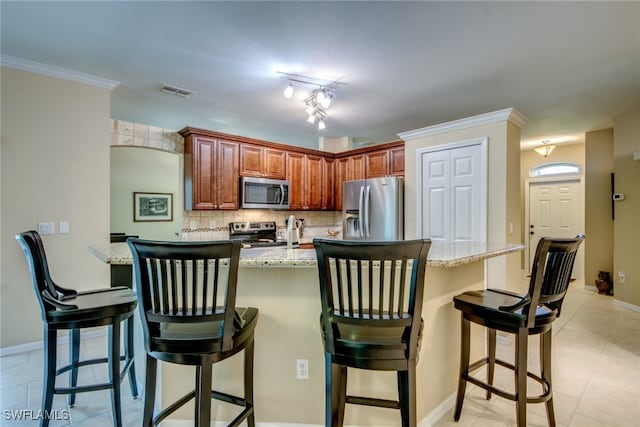 kitchen with ornamental molding, a kitchen breakfast bar, stainless steel appliances, light stone countertops, and decorative backsplash