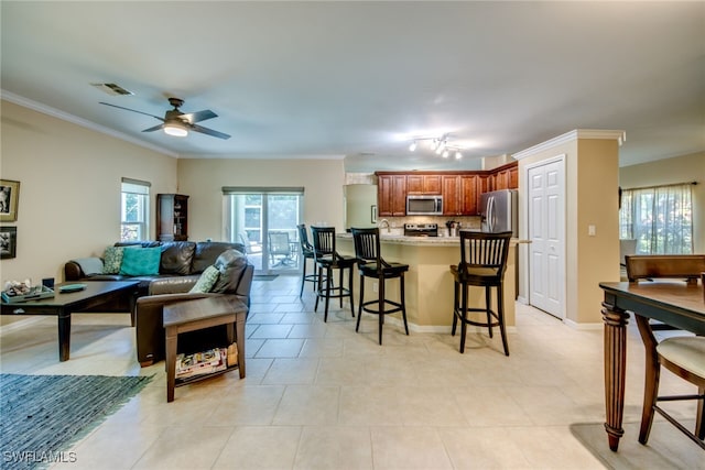 kitchen with light tile patterned floors, a breakfast bar, ceiling fan, appliances with stainless steel finishes, and ornamental molding