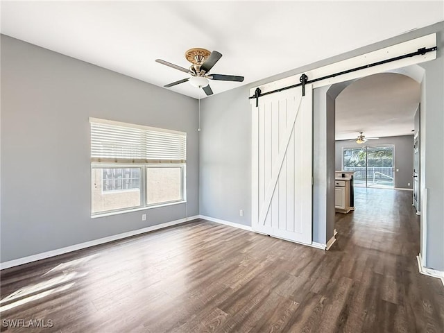 unfurnished room with a barn door, dark hardwood / wood-style floors, and ceiling fan