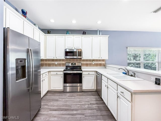 kitchen featuring sink, appliances with stainless steel finishes, wood-type flooring, white cabinets, and decorative backsplash