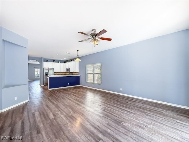 unfurnished living room featuring ceiling fan, a wealth of natural light, and dark hardwood / wood-style flooring