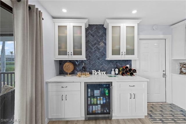 bar with wine cooler, white cabinetry, tasteful backsplash, and light wood-type flooring