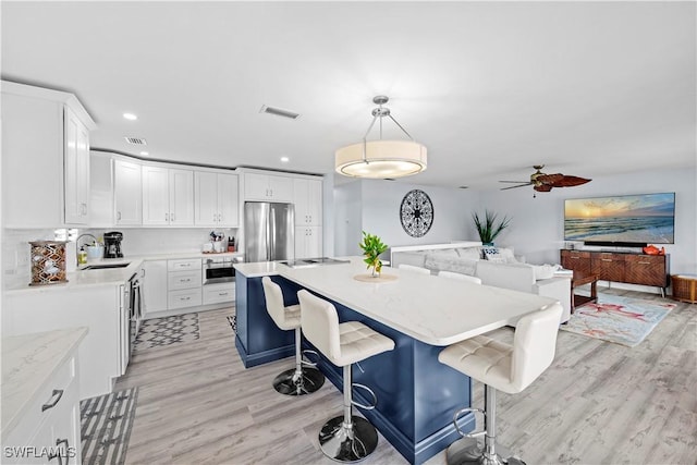 kitchen featuring sink, a breakfast bar area, stainless steel refrigerator, white cabinets, and decorative light fixtures