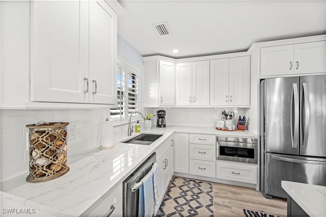 kitchen with appliances with stainless steel finishes, tasteful backsplash, sink, white cabinets, and light stone countertops