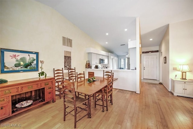 dining room with high vaulted ceiling and light hardwood / wood-style flooring