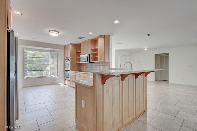 kitchen featuring appliances with stainless steel finishes, a breakfast bar, backsplash, light stone counters, and light brown cabinets