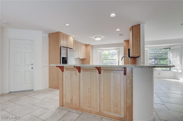 kitchen with a breakfast bar area, stainless steel fridge with ice dispenser, light tile patterned floors, light brown cabinets, and kitchen peninsula